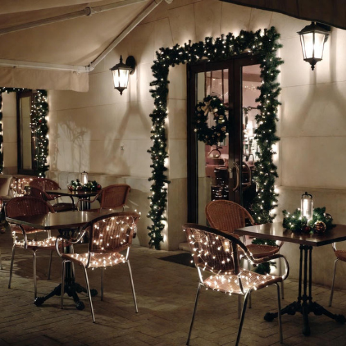 Restaurant outdoor seating decorated with LED-wrapped tables, garlands, and subtle lighting for festive holiday ambiance.