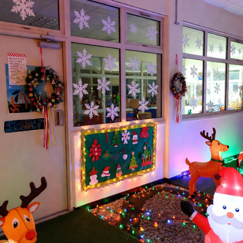 School entrance decorated with paper snowflakes, student-made wreaths, and outdoor lights for a festive classroom display.