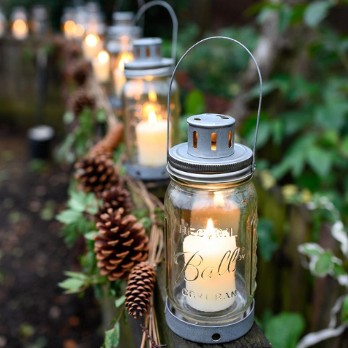 Mason jar lanterns glowing on outdoor fence with pinecone garlands, showcasing eco-friendly DIY Christmas decorations.