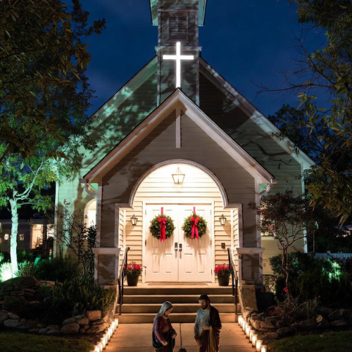 Church front yard with nativity scene, evergreen wreaths, and pathway candles creating an inviting Christmas display.
