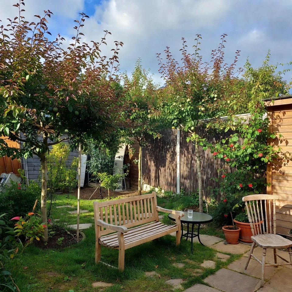 Cozy garden corner with rattan chairs, small coffee table, and lush green plants surrounding the seating area.