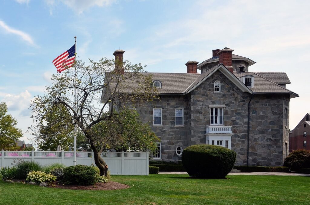 Modern front yard featuring a wood, concrete, and stone planting bed with minimalist plants, a clean walkway, and decorative lighting