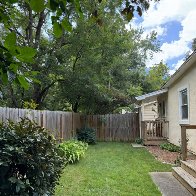 Backyard of a typical USA home with green lawn, wooden deck, outdoor seating, and surrounding fence.