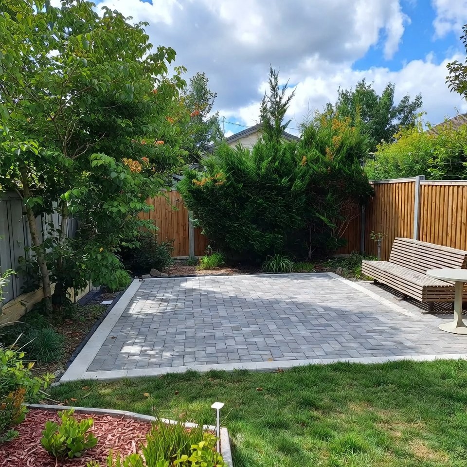 Backyard with paver patio layout featuring a patterned stone surface, outdoor seating area, and surrounding garden plants.