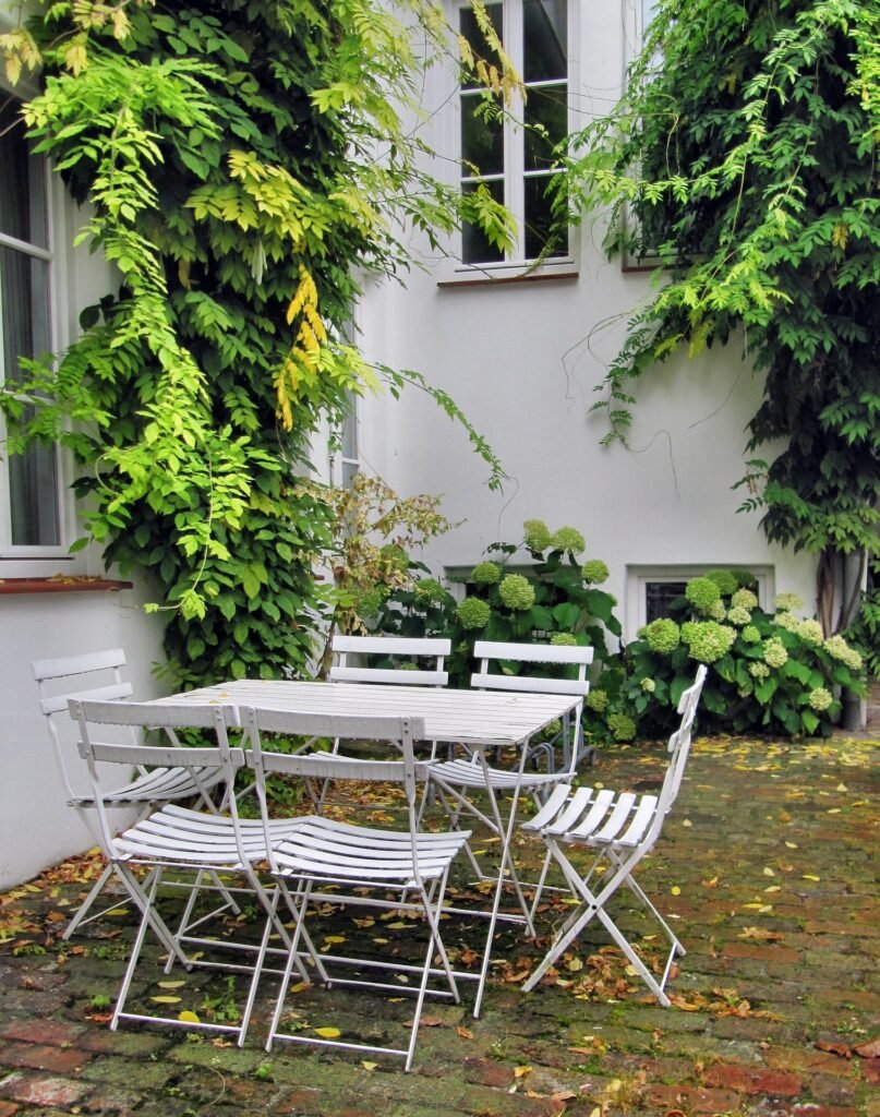 Evening view of a backyard garden with wooden deck, seating area, string lights, and landscaped greenery.