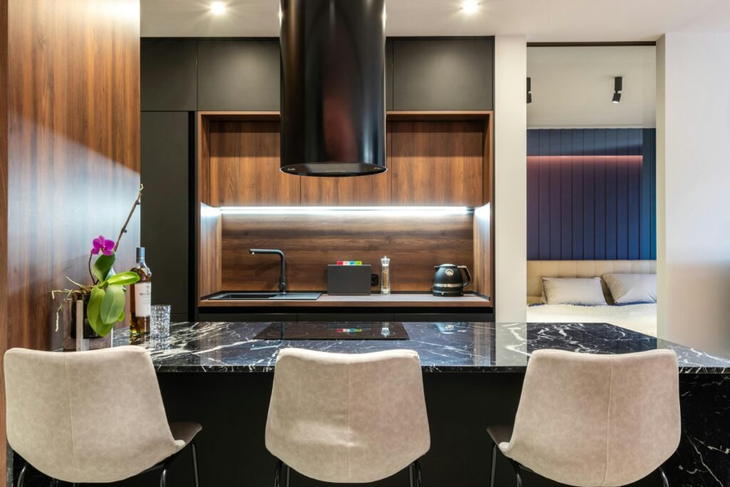 Modern kitchen with a kitchen range exhaust hood above the stove, dark cabinets, and a clean backsplash.