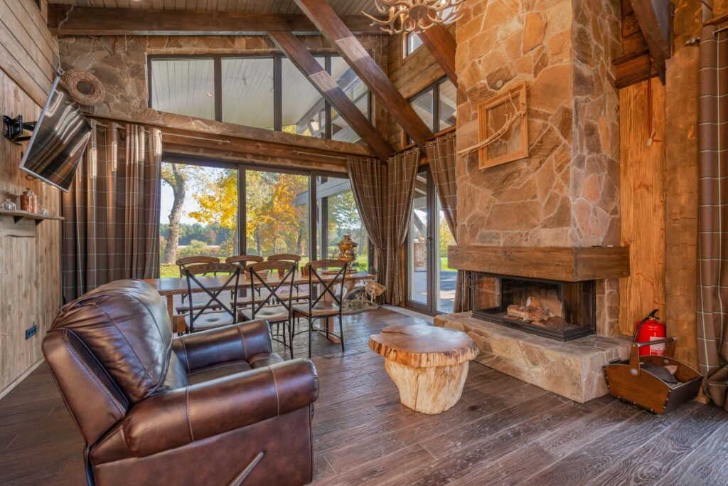 Warm and cozy living room featuring reclaimed wood furniture, leather seating, stone details, vintage accessories, and earthy color tones.