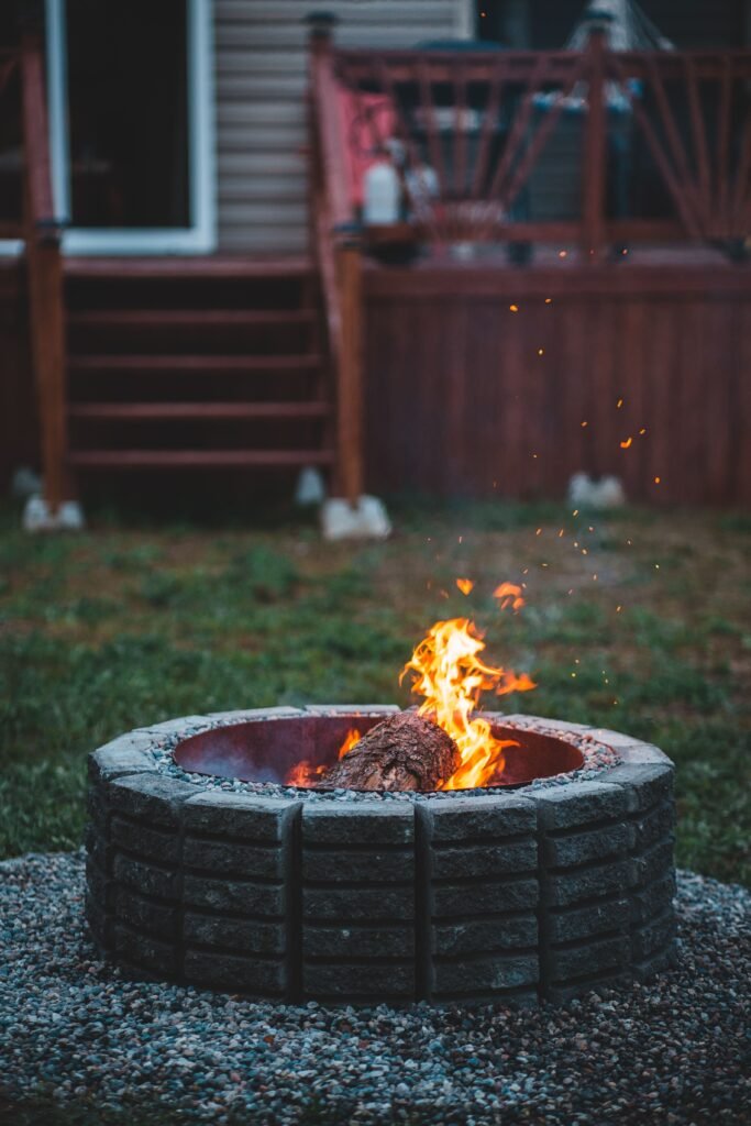 Outdoor fire pit lounge area with comfortable seating, mulch landscaping, and decorative plants, showcasing low maintenance backyard ideas without grass.