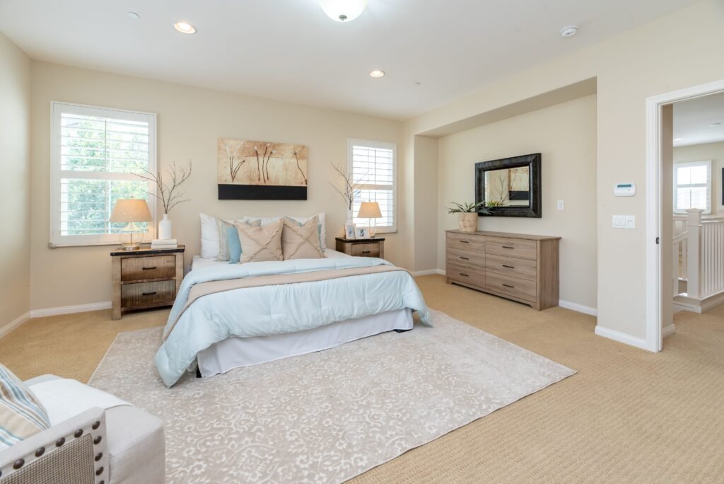 Modern master bedroom with light colors, featuring a king-size bed, white walls, soft gray accents, natural light, and elegant contemporary furniture.