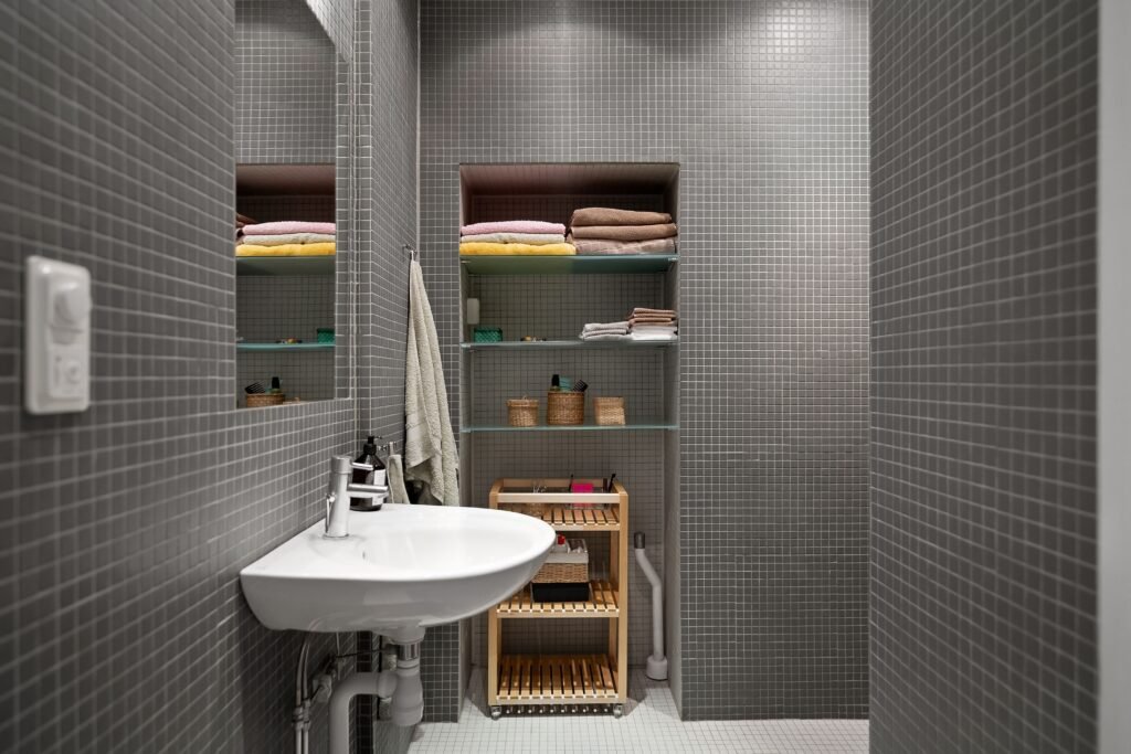 Modern bathroom with open shelving displaying neatly arranged towels, decor, and everyday essentials in a stylish layout.