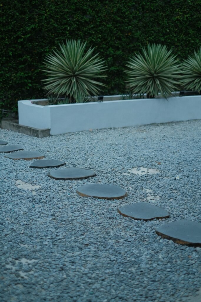 Low maintenance backyard ideas without grass showcasing a modern stone patio, decorative gravel, raised garden beds, and drought-tolerant landscaping