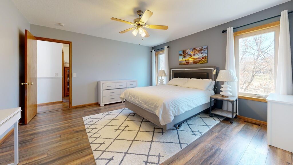 Modern master bedroom with large area rugs, featuring soft textured carpet, neutral tones, stylish furniture, and a cozy contemporary layout.