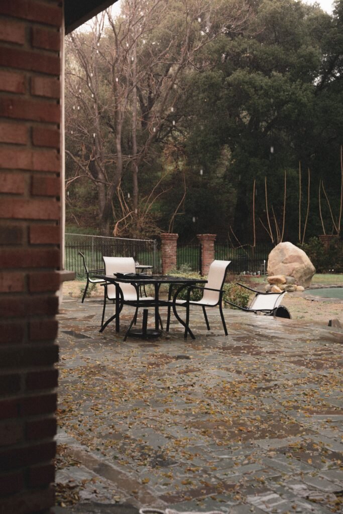 Low maintenance backyards without grass designed for a rainy climate, featuring gravel landscaping, stone pathways, cozy outdoor seating, a fire pit, weather-resistant furniture, drainage-friendly surfaces, and lush greenery illuminated by warm landscape lighting.