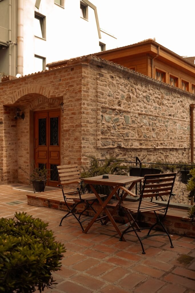 Low maintenance backyard ideas without grass featuring a Mediterranean courtyard design with stone paving, terracotta accents, olive-style plants, and warm rustic textures.
